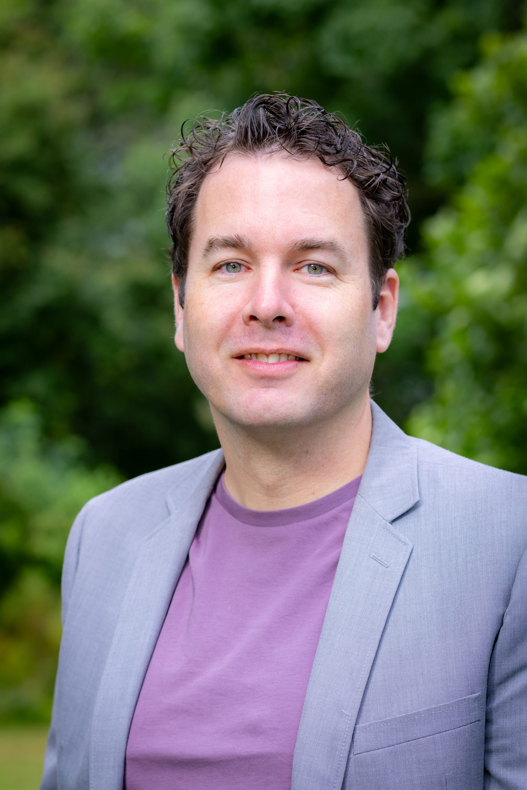 Wethouder Mark Versteeg poseert in lichtblauw pak met paar shirt glimlachend in de buitenlucht