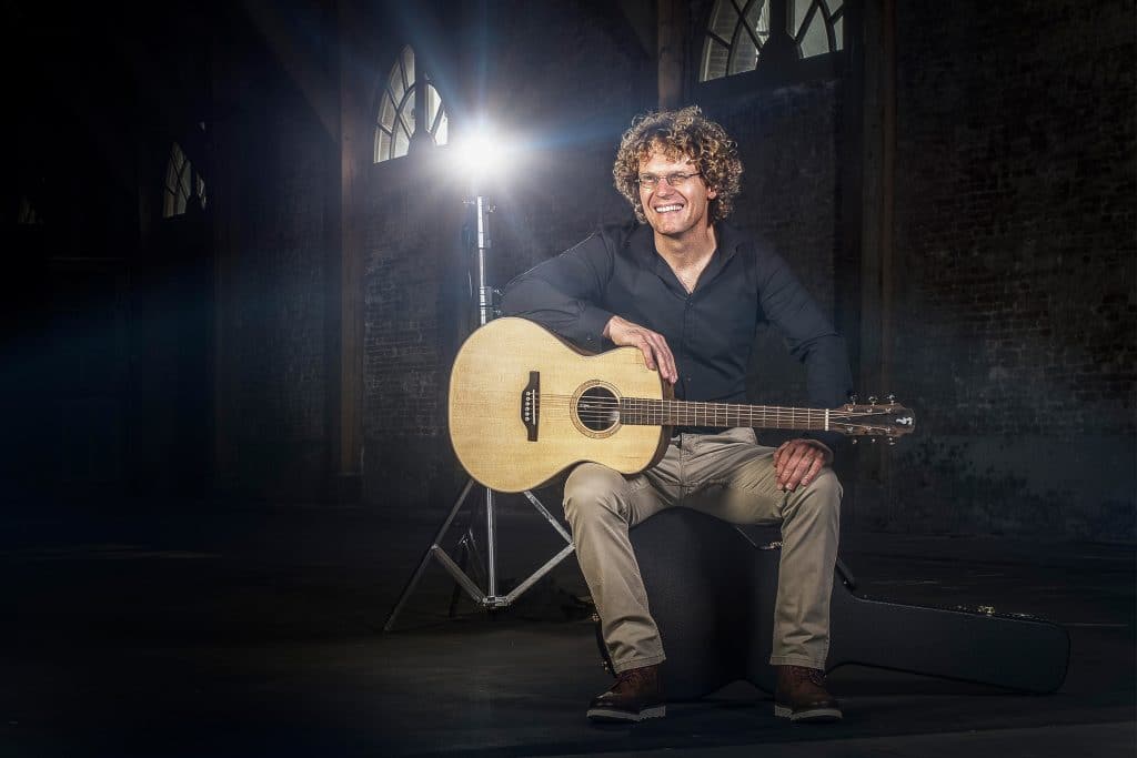 Dick Raat op een kruk met zijn gitaar.