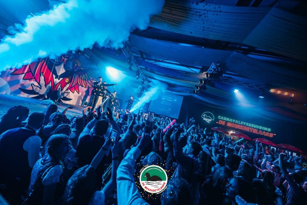 Carnaval C.V. De Meerkoetelaars met een muziekoptreden op een podium. Vooraan publiek en links een rookmachine