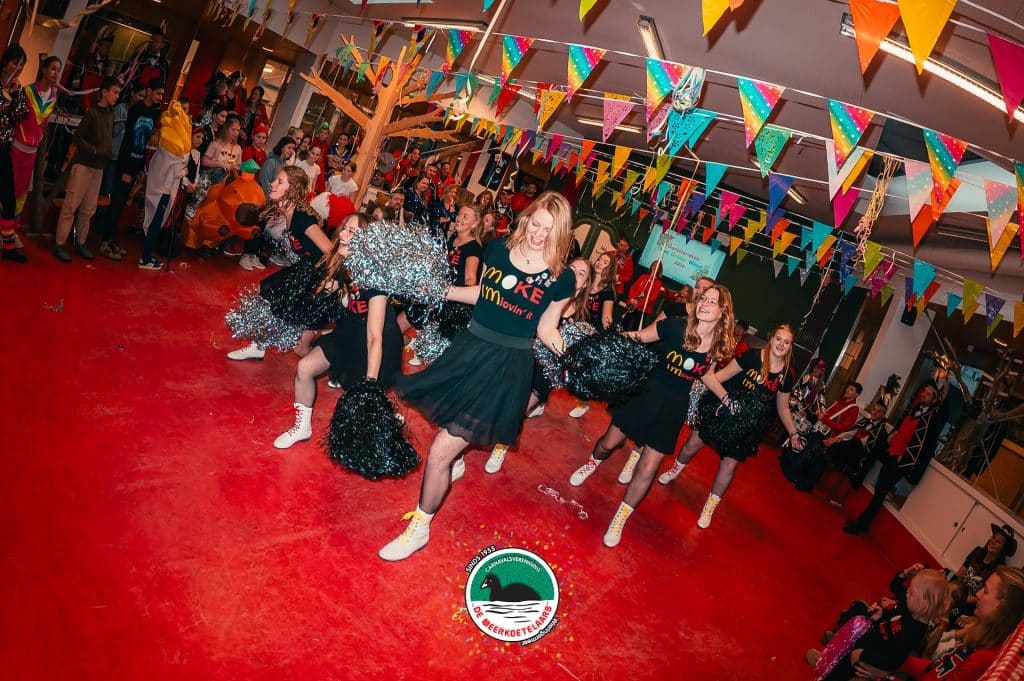 Dansers gekleed in zwart tijdens Carnaval C.V. De Meerkoetelaars op een rood kleed met vlaggetjes erboven